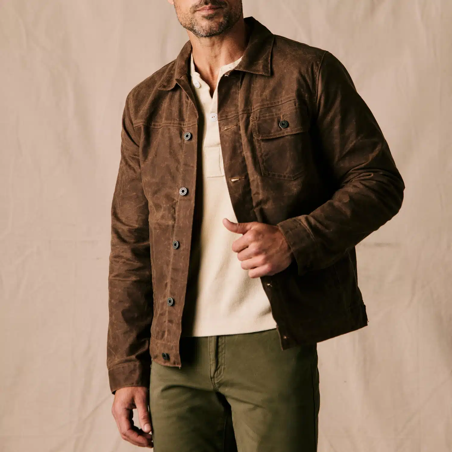 Man wearing a brown jacket over a beige shirt and olive pants, highlighting modern workwear fashion.